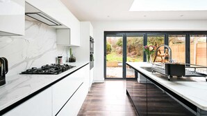 A modern kitchen with a marble countertop, black appliances, and a view of the outdoors through large windows. - 3 Bed House Near Epping Forest Greater London (London)