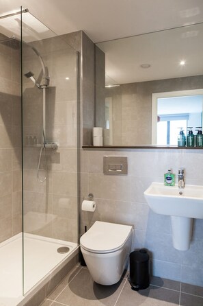 A modern bathroom with a glass-enclosed shower, a white toilet, a sink, and a mirror above the sink. - 2 Bed Flats Near Station & City Centre - Sleeps 6 (Leeds)