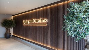 Een receptiegedeelte met een wand van houten panelen, een potplant en een bordje met de tekst 'Springwell Gardens'.