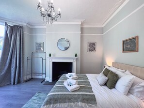 A bedroom with a bed, a fireplace, a chandelier, and artwork on the walls. - 6 Bedroom Victorian Townhouse in Central Harrogate (Harrogate)