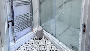 Ein modernes Badezimmer mit Duschkabine aus Glas, chromfarbenem Handtuchhalter und fliesenbelagtem Boden.
