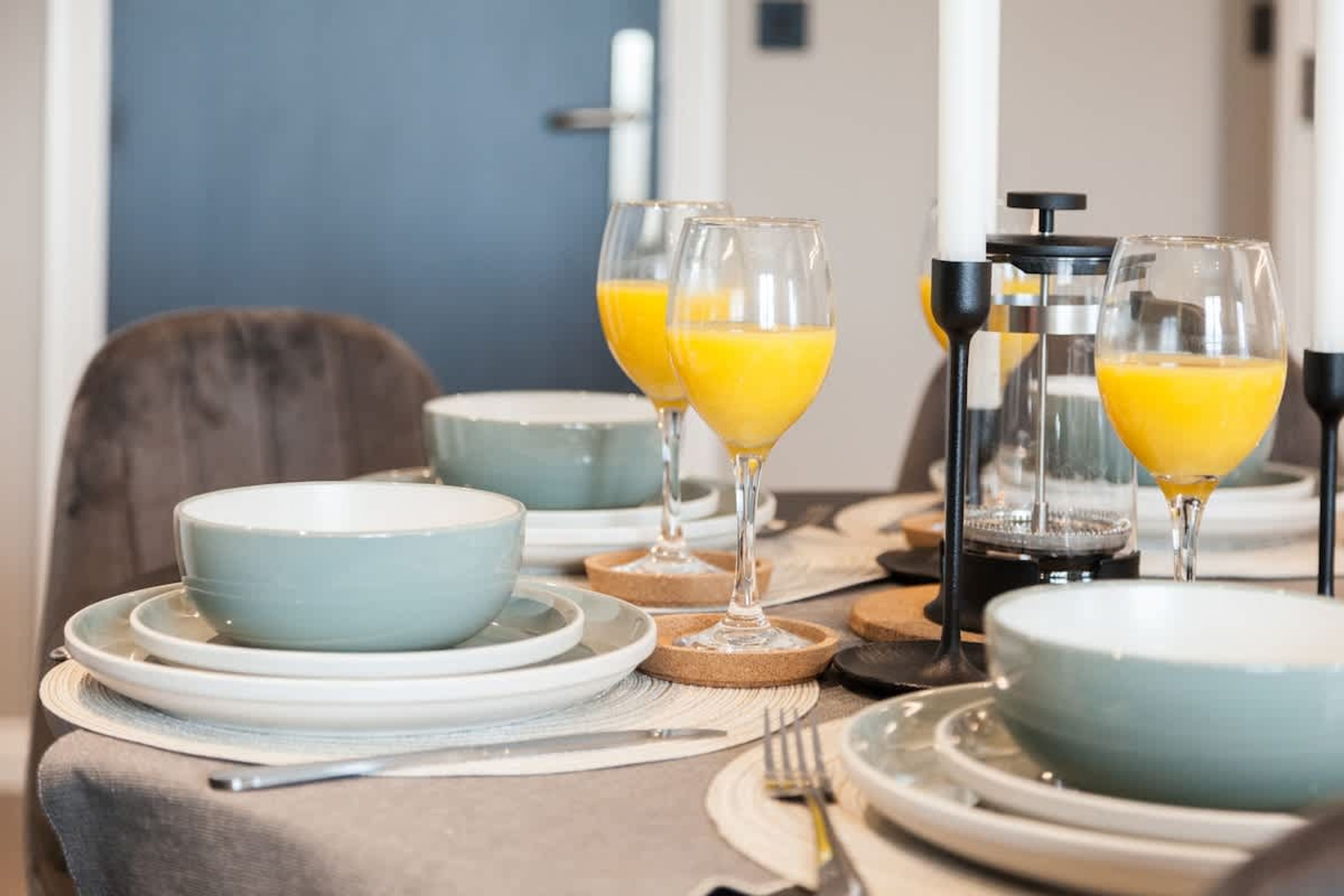 A dining table set with plates, bowls, glasses, and a coffee maker.