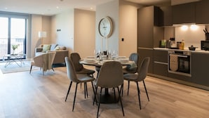 A modern kitchen with a dining area, a round table set for four, and a large wall clock. - 3 Bed Flats Near Station City Centre - Sleeps 6 (Leeds)