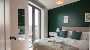 A bedroom with a bed, a nightstand, a lamp, and a window. - 3 Bed Flats Near Station City Centre - Sleeps 6 (Leeds)