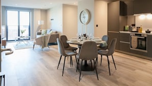 A modern living room with a dining area, a large window, and a kitchen with dark cabinets. - 3 Bed Flats Near Station City Centre - Sleeps 6 (Leeds)