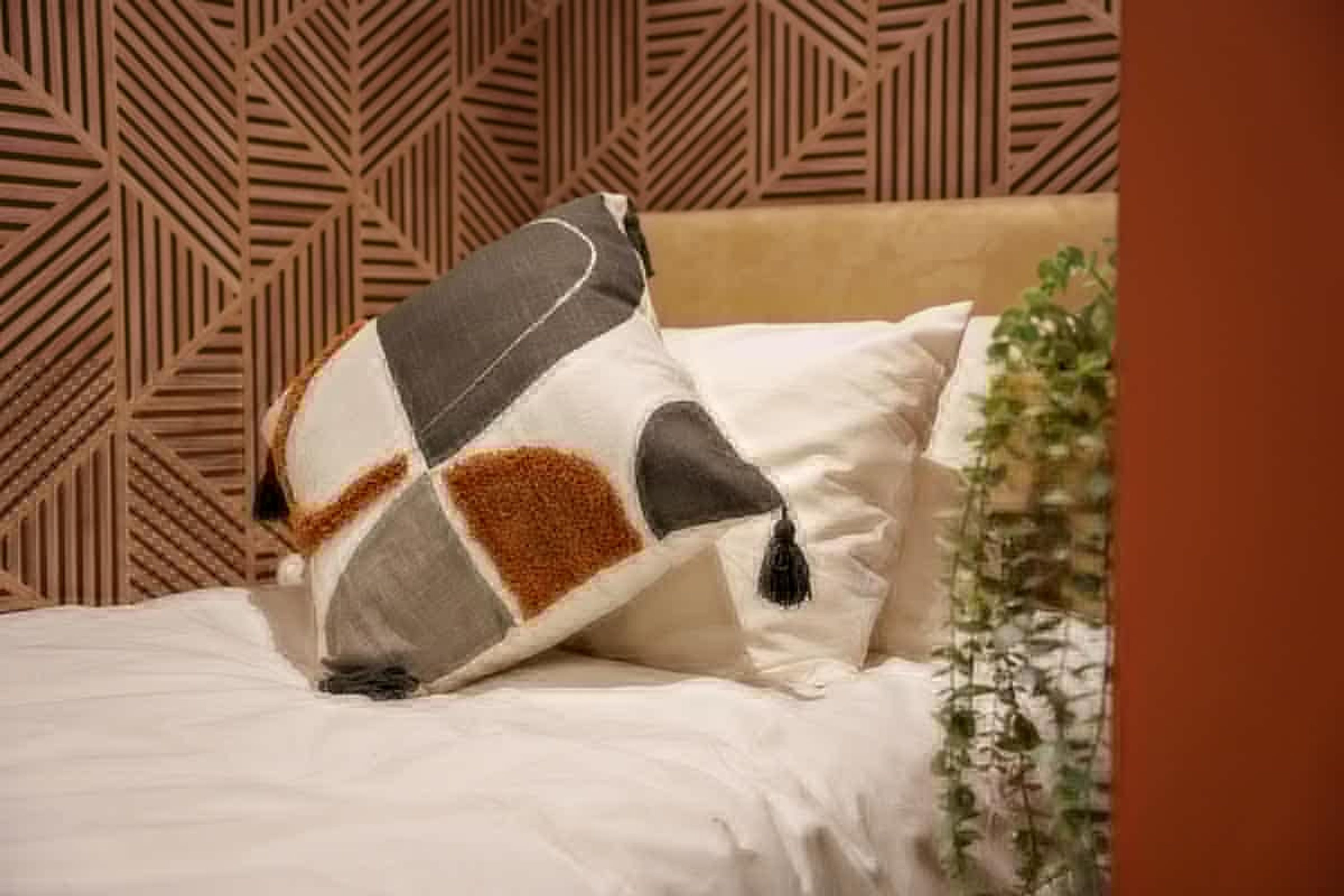 Een bed met gekleurde kussens en een geometrisch patroon op de muur.