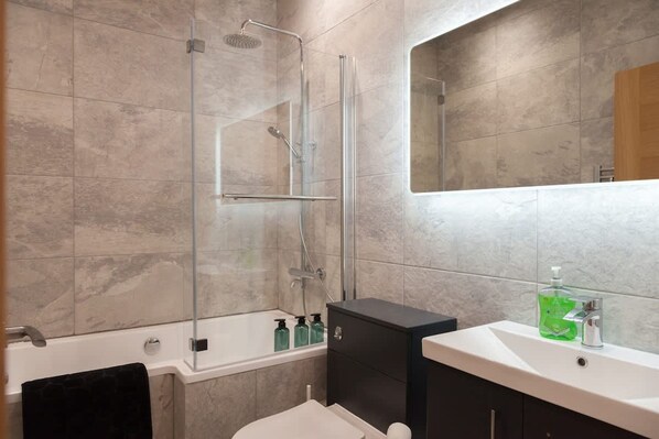 A modern bathroom with a glass-enclosed shower, a white bathtub, a black cabinet, and a white sink with a mirror above it.