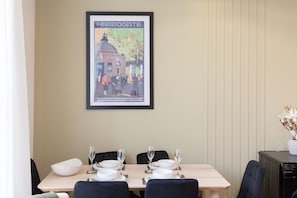 Un coin repas avec une table dressée pour quatre personnes, une affiche encadrée au mur et un lave-vaisselle dans un coin.
