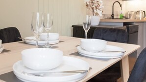 A dining table set with white plates, bowls, and wine glasses, with a modern kitchen in the background. - Bright 2-bed Flat - Harrogate Town Centre - 4 Bed (Harrogate)