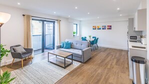 A modern living room with a sofa, coffee table, and a dining area with chairs. - Brighton Penthouse Apartment Near Beach & Kemptown (Brighton)