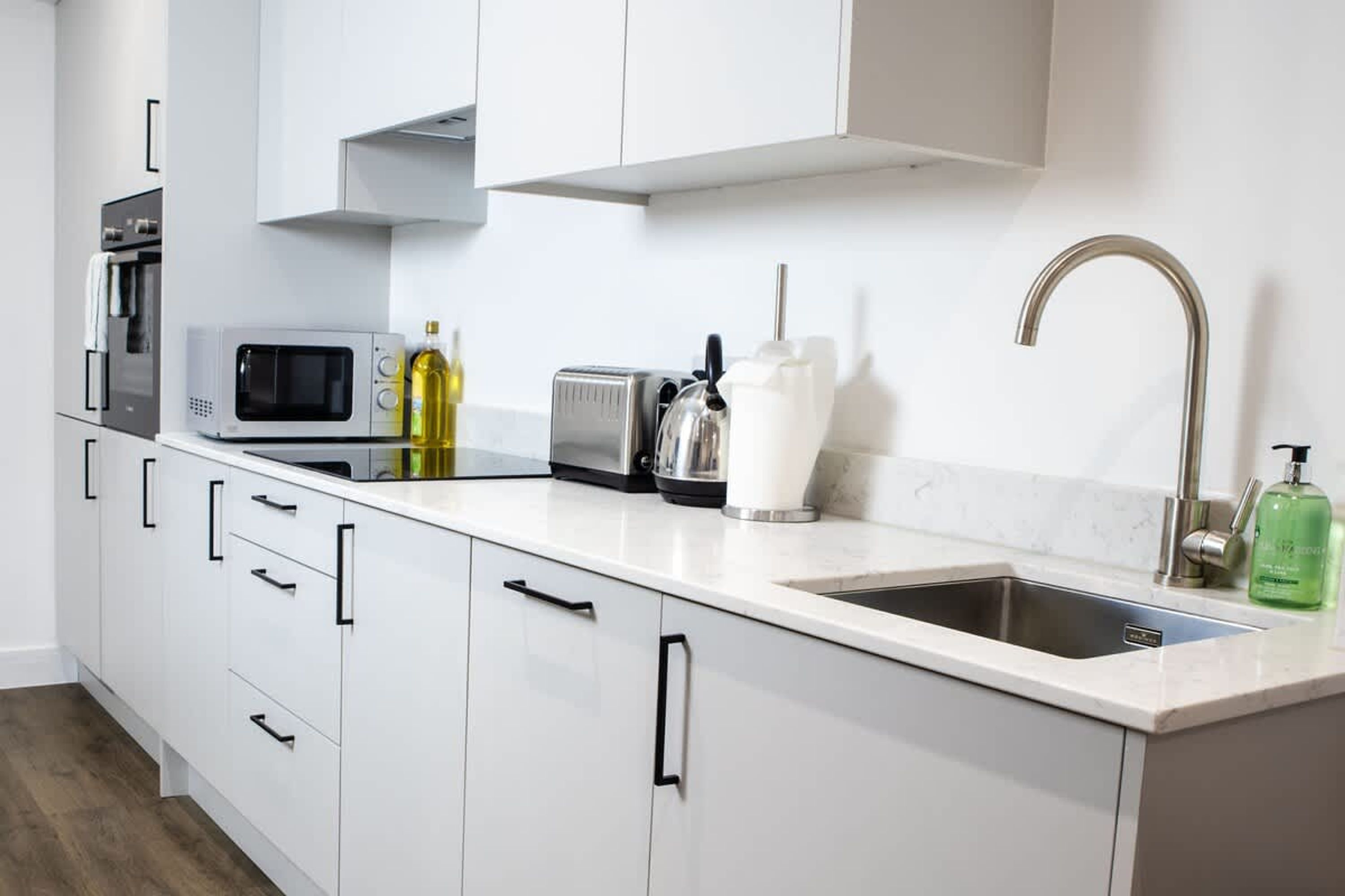 A modern kitchen with white cabinets, a stainless steel sink, a microwave, a toaster, and a kettle.