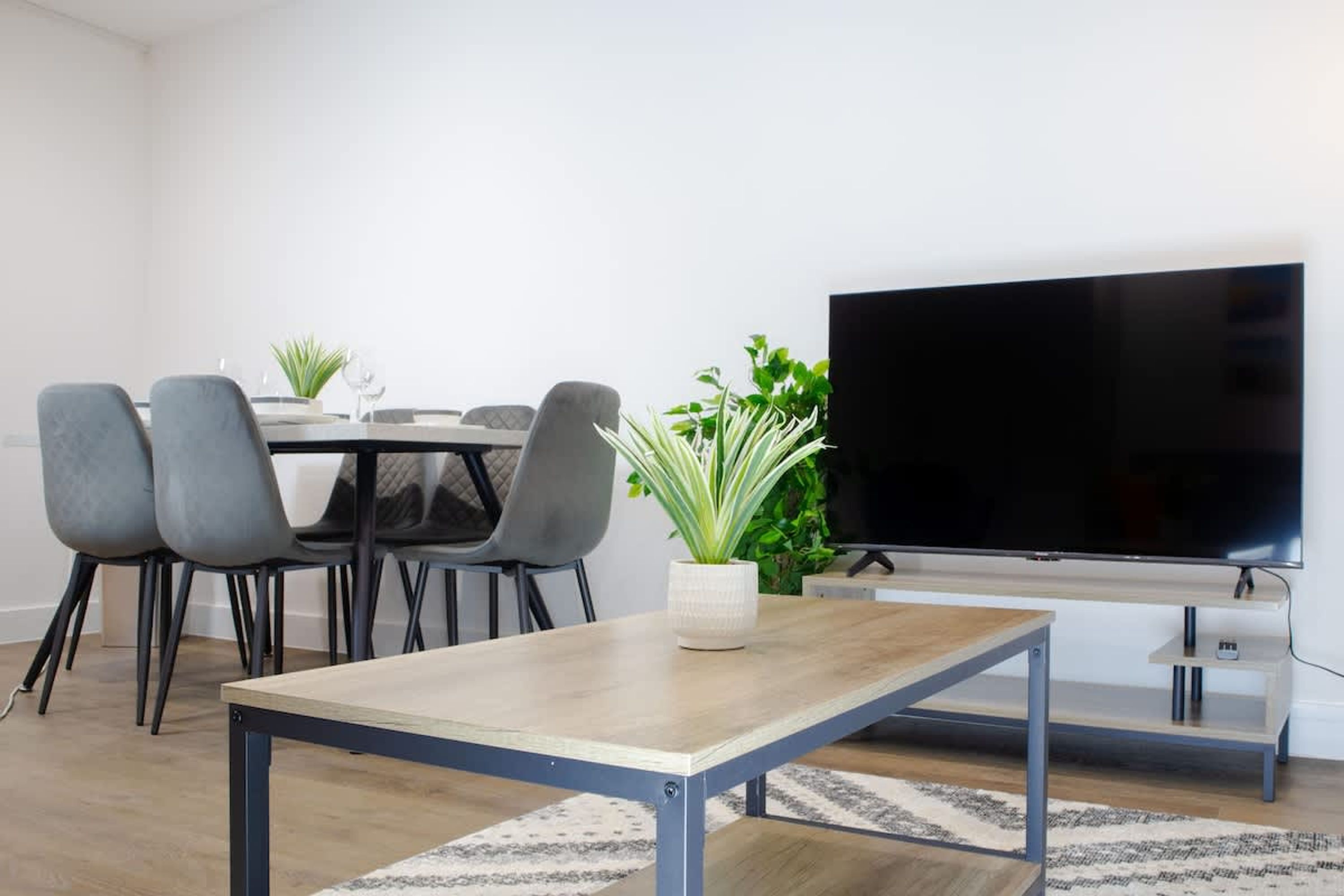 A modern living room with a dining table, chairs, a TV, and two potted plants.