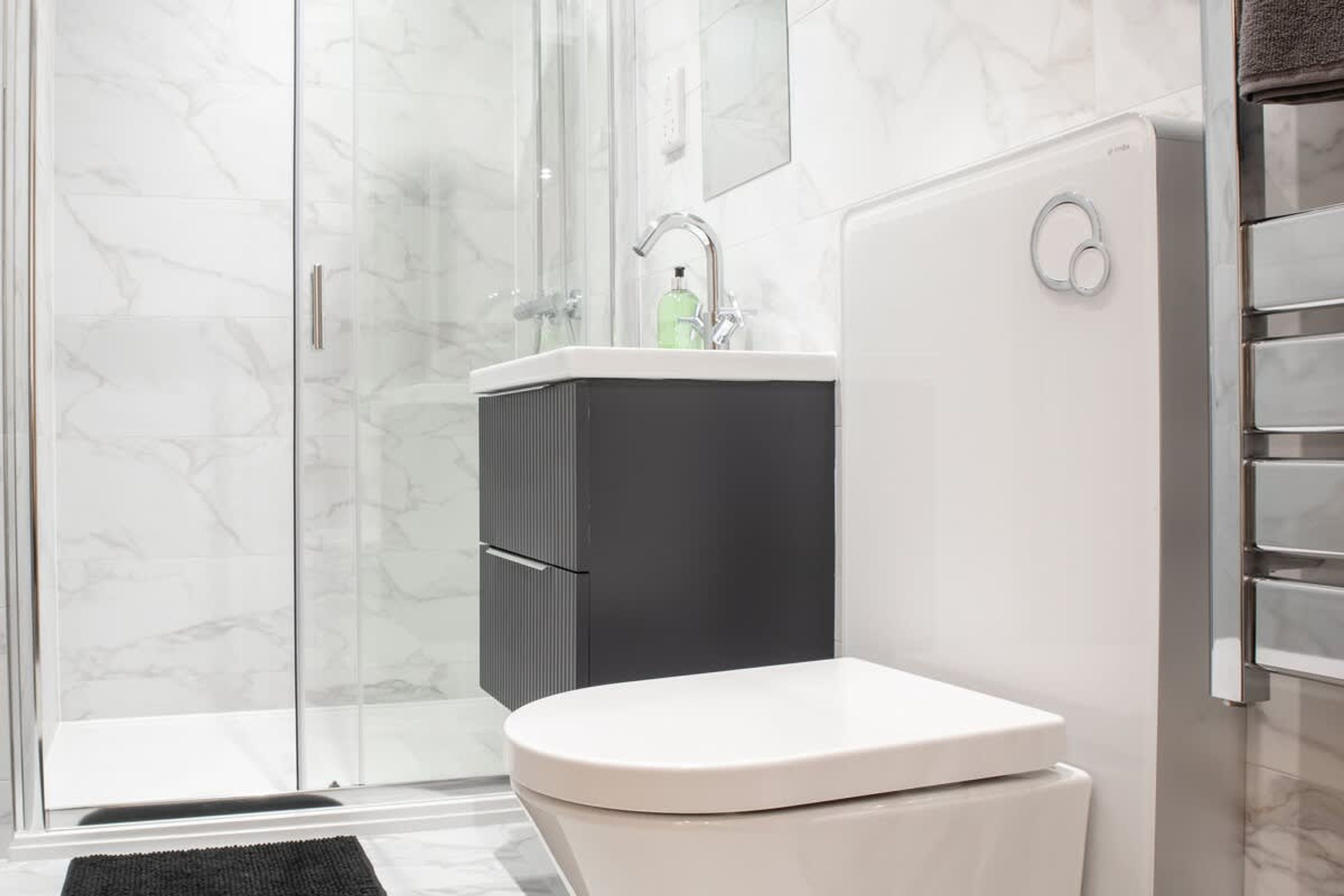Un baño moderno con cabina de ducha de vidrio, un inodoro blanco y un mueble negro.