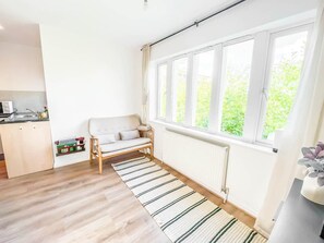 A bright room with a sofa, a radiator, a window, and a kitchen area. - Private 2-bed Duplex Near Headingly w Parking (Leeds)