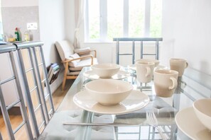 Une table à manger avec des bols et des tasses, une chaise et une fenêtre laissant entrer la lumière naturelle.