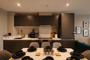 Une cuisine moderne avec des meubles de couleur sombre, un four à micro-ondes et un coin repas avec une table dressée pour quatre personnes.