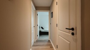 Un couloir étroit, doté d’un plancher en bois, mène à une chambre à coucher qui contient un lit et une table de chevet.