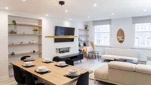 A modern living room with a dining area, a sofa, and a TV mounted on the wall. - Central Leeds Apartment by Station - Sleeps 7 (Leeds)