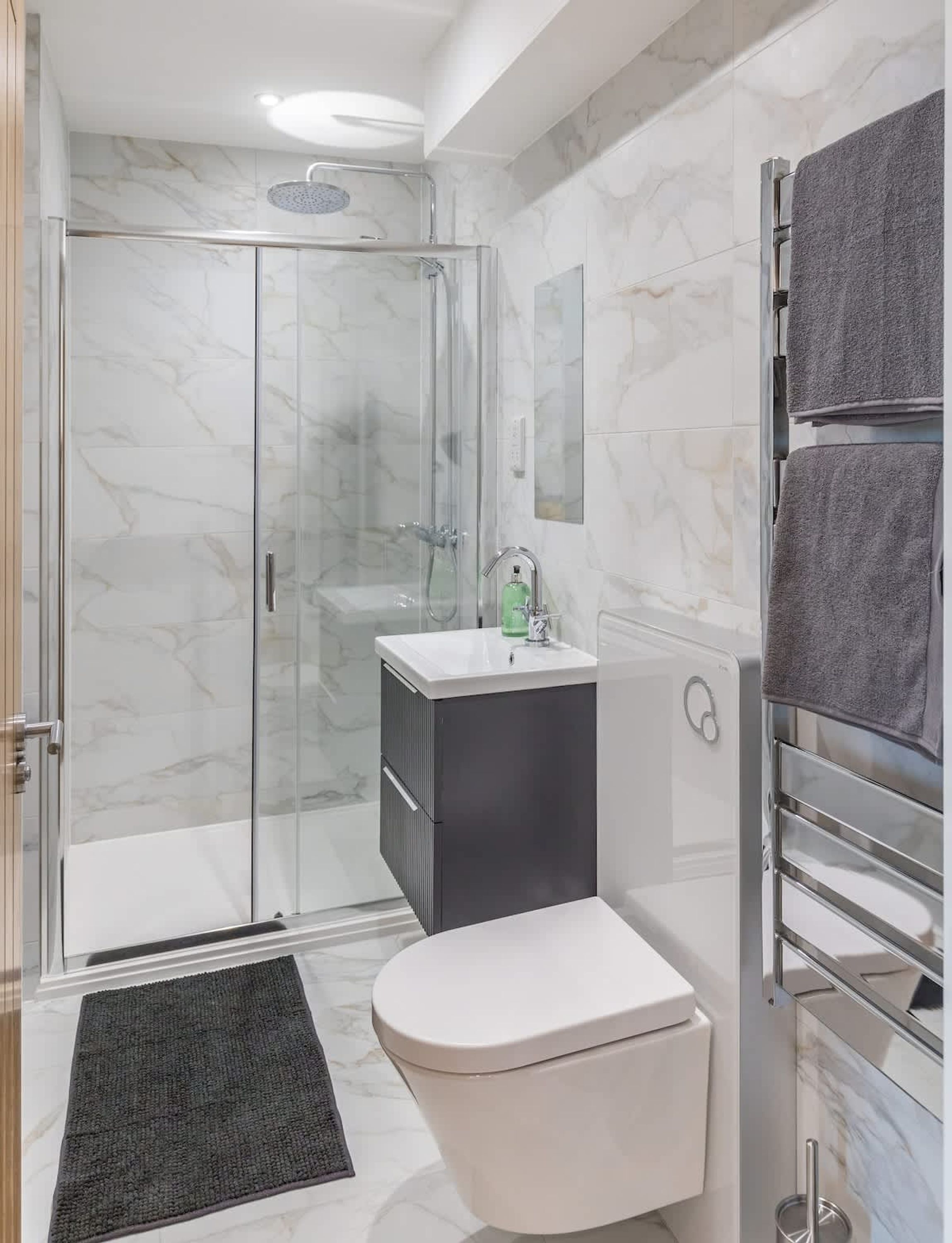 A modern bathroom with a glass-enclosed shower, a white toilet, a sink with a mirror, and a towel rack.