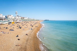 A beach with people sunbathing and swimming, a pier with buildings, and a clear sky.