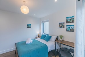 A bedroom with a bed, bedside table, lamp, and artwork on the wall.