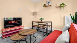 A living room with a TV, a red sofa, a coffee table, a small table with a plant, and two wall-mounted shelves with plants. - Modern 3BR Manchester Stay With Parking Wifi (Manchester)