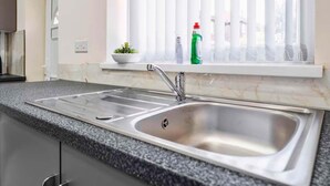 A kitchen with a stainless steel sink, granite countertop, and a window with blinds. - Modern 3BR Manchester Stay With Parking Wifi (Manchester)