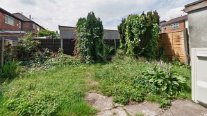 A residential backyard with a wooden fence, a variety of plants, and a stone pathway. - Modern 3BR Manchester Stay With Parking Wifi (Manchester)