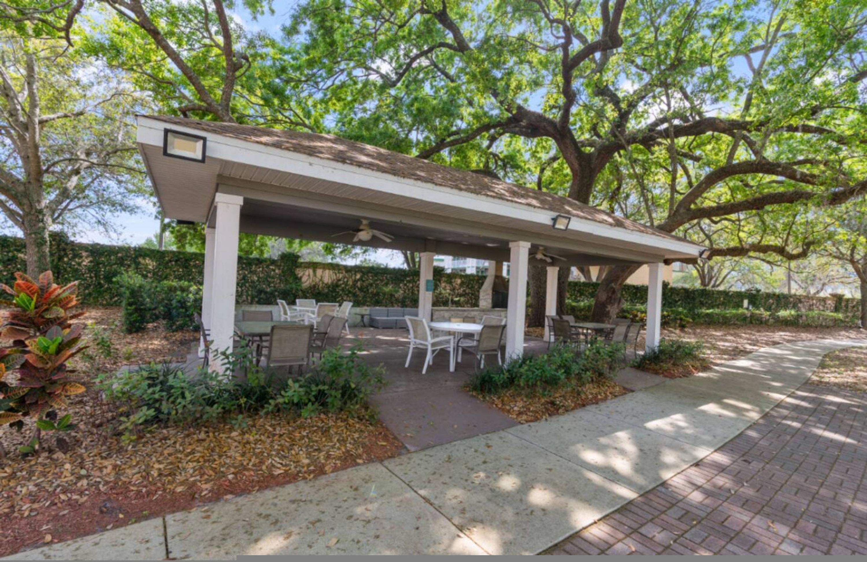 A covered patio area with outdoor seating, surrounded by trees and greenery.