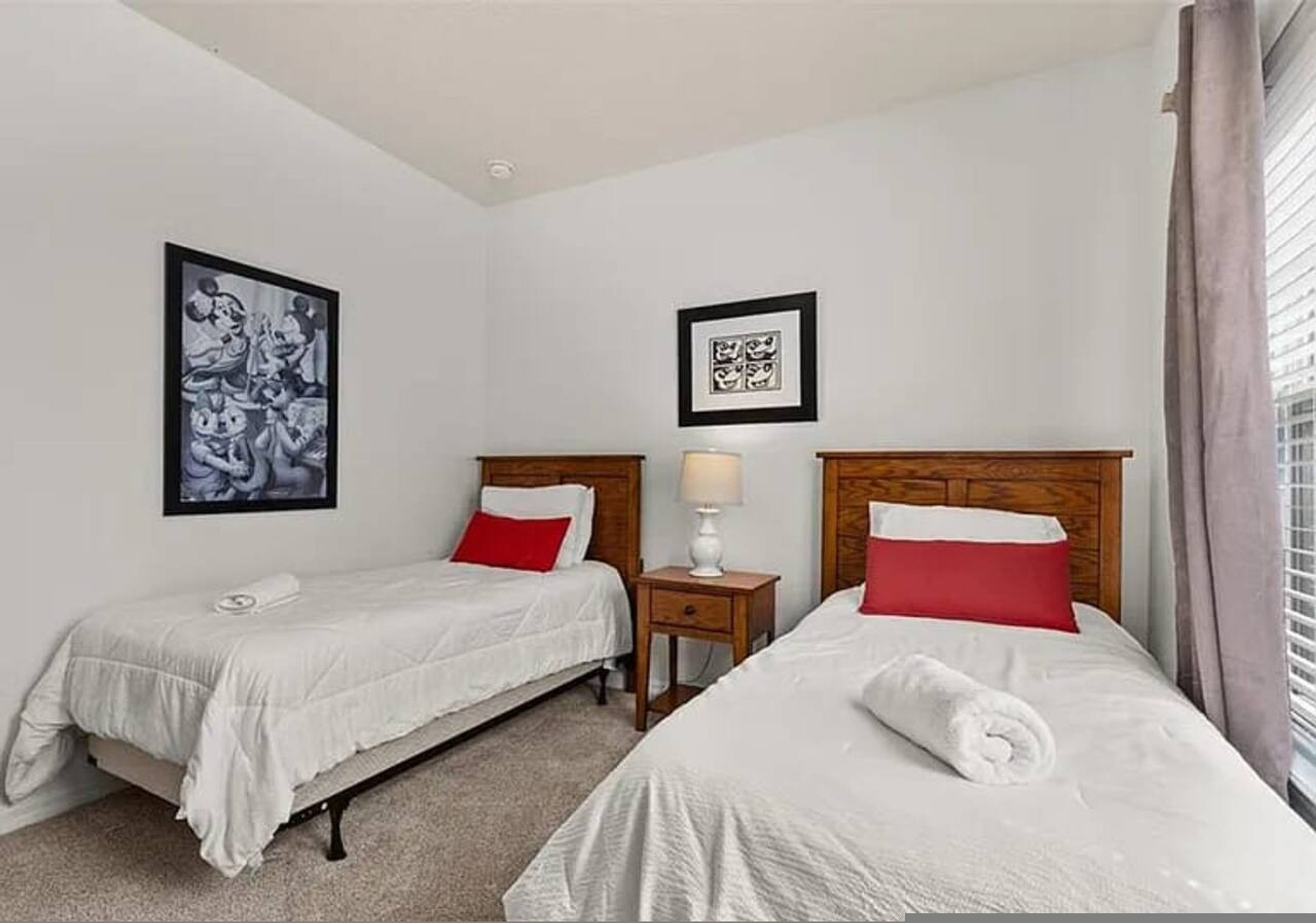 A hotel room with two single beds, a nightstand with a lamp, and two framed pictures on the walls.