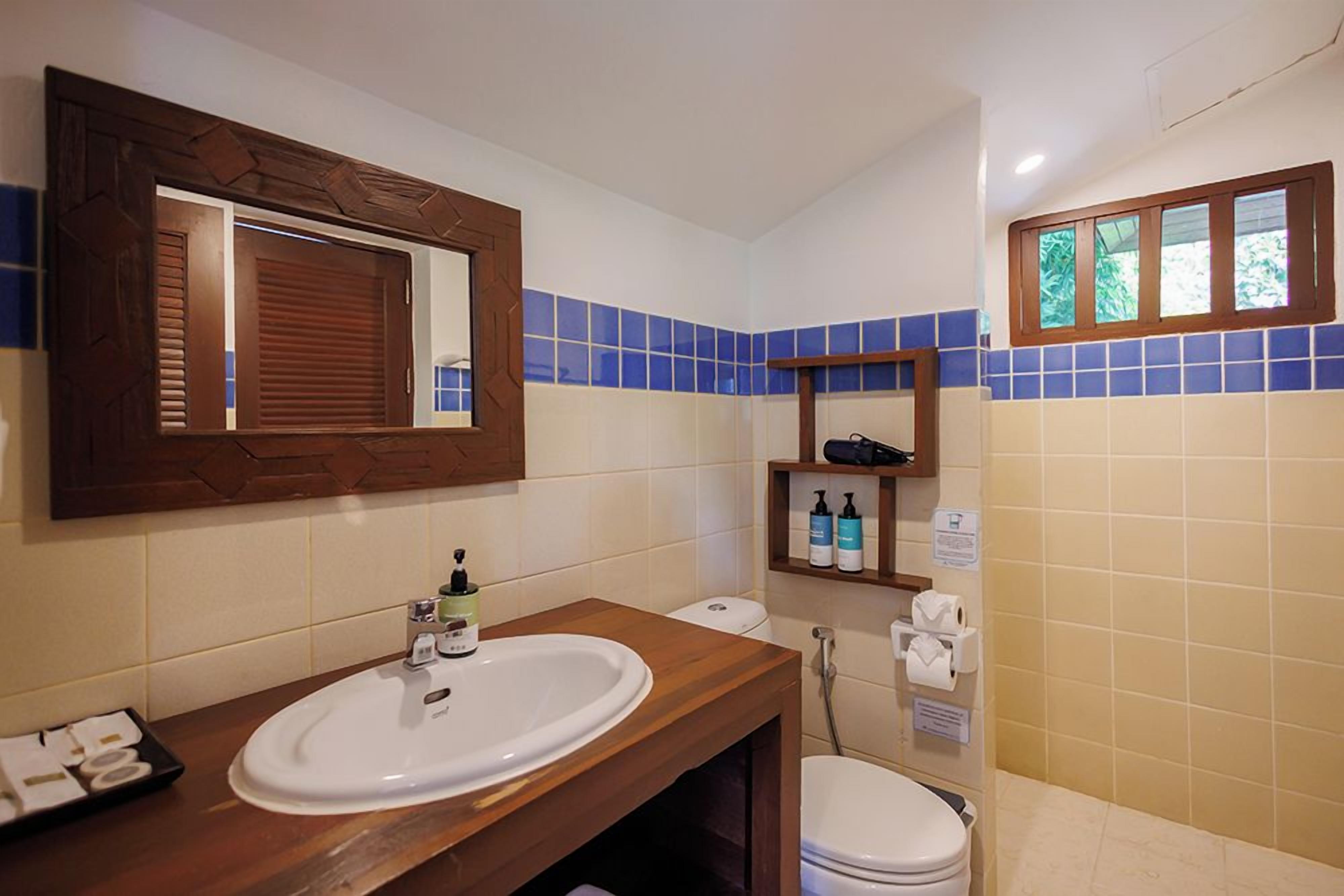 A bathroom with a wooden vanity, a white sink, a mirror, and a toilet.