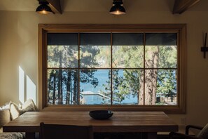 A dining area with a large window, wooden table, and chairs. - Aurora Hygge - Lakefront Luxury Home with Sauna, Hot Tub, Lake Views (Big Bear Lake)