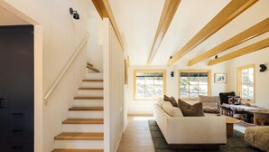 A staircase leading to a second floor, a living room with a sofa and a coffee table, and a bookshelf. - Aurora Hygge - Lakefront Luxury Home with Sauna, Hot Tub, Lake Views (Big Bear Lake)