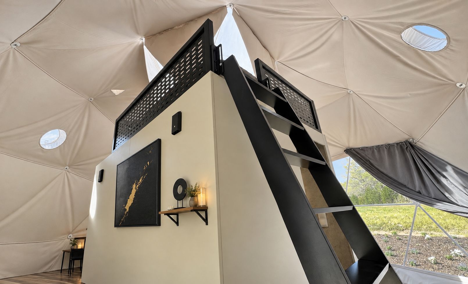 A tent with a black metal staircase, a framed artwork, and a small shelf with decorative items.