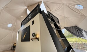 Una carpa con una escalera metálica negra, una obra de arte enmarco y un estante pequeño con adornos.