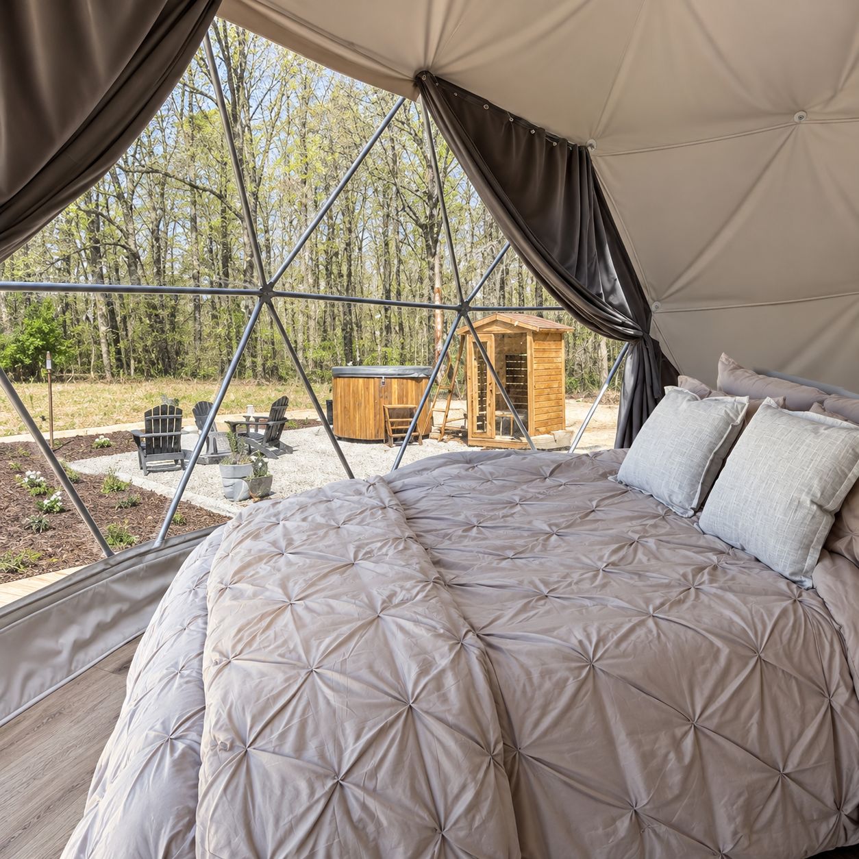 A tent with a bed, a hot tub, and a wooden structure in the background.