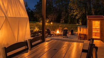 An outdoor patio with a wooden table and chairs, string lights, a tent, and a small wooden structure.