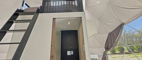 Een tentaccomodatie met een ladder naar een deur, een klein raam en uitzicht op de omgeving.