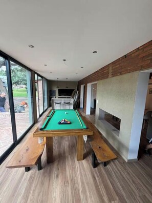 A pool table with a green felt surface, wooden benches, and a brick wall.