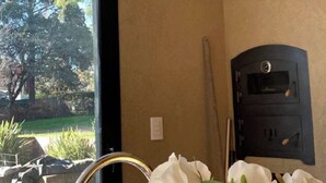 Una habitación con un ventanal grande, un calentador negro y un florero blanco.