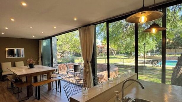 Una cocina moderna con una isla grande, un comedor con mesa y sillas, y ventanas amplias con vistas al exterior.