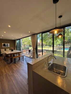 A modern kitchen with a large island, a dining area with a table and chairs, and large windows offering a view of the outdoors.