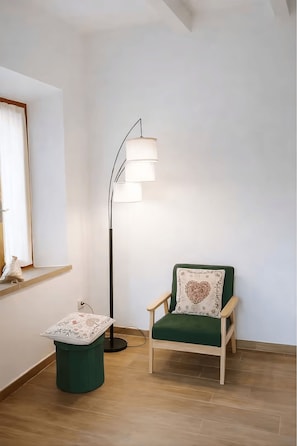 Ein Zimmer mit einem grünen Sessel, einer Stehlampe und einem kleinen Tisch mit gemustertem Tischlein.