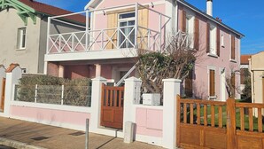 Ein zweistöckiges Haus mit Balkon, geschlossenem Eingangsbereich und einem kleinen Garten.
