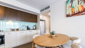 A modern kitchen with white cabinets, a wooden dining table, and a potted plant. - Waterfront Lagoon Suite: 1 Bed Apt (Darwin)