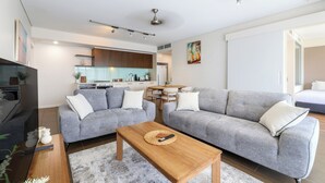 A modern living room with grey sofas, a wooden coffee table, and a kitchen in the background. - Waterfront Lagoon Suite: 1 Bed Apt (Darwin)