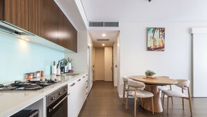 A modern kitchen with a dining area, featuring a stove, oven, and dining table with chairs. - Waterfront Lagoon Suite: 1 Bed Apt (Darwin)
