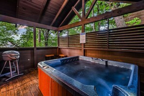 A hot tub with a wooden deck and a grill, surrounded by trees. - Silver Maple Summit 2 Bedroom Cabin (Gatlinburg)