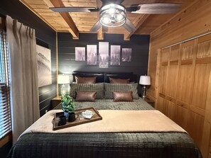 A bedroom with a bed, headboard, bedside tables, lamps, a ceiling fan, and wall art. - Silver Maple Summit 2 Bedroom Cabin (Gatlinburg)