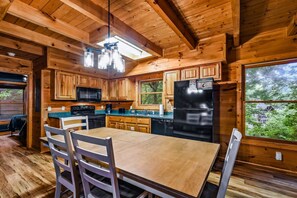 A wooden cabin interior with a dining area, kitchen, and large windows. - Silver Maple Summit 2 Bedroom Cabin (Gatlinburg)
